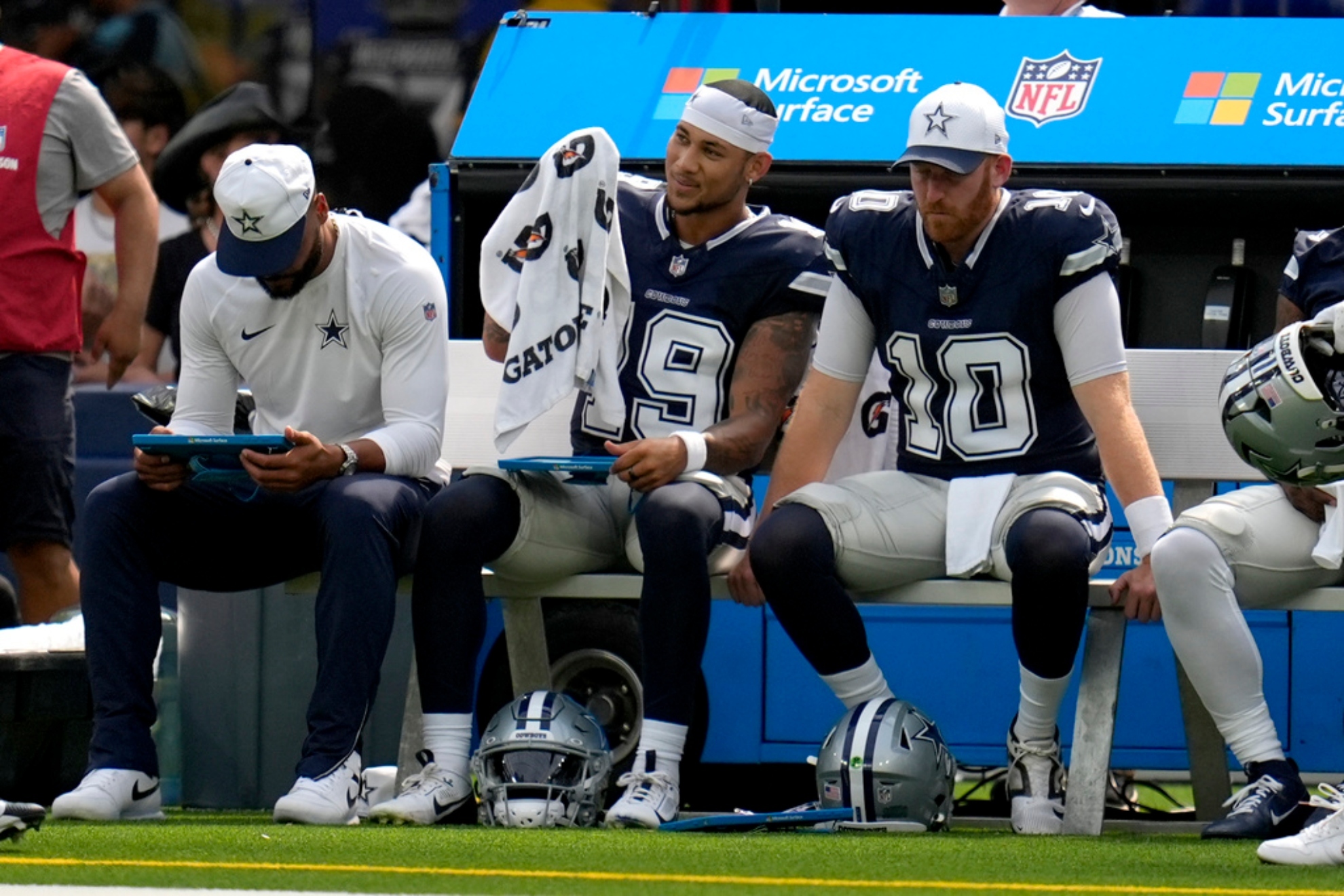 Dallas Cowboys QB Trey Lance, center, smiles as he sits on the bench between Dak Prescott, left, and Cooper Rush (10).