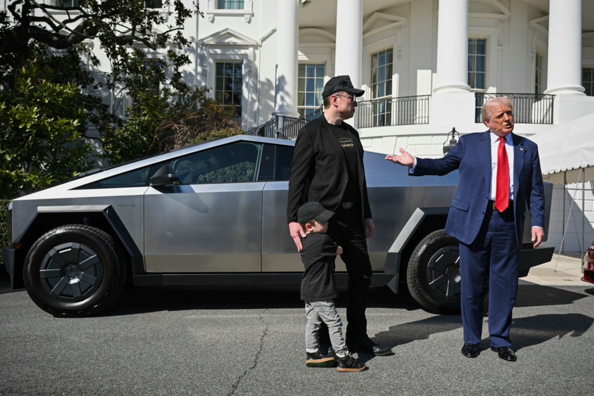 President Donald Trump and Tesla CEO Elon Musk, along with his son X � A-Xii, speaks to reporters by a Tesla vehicle.