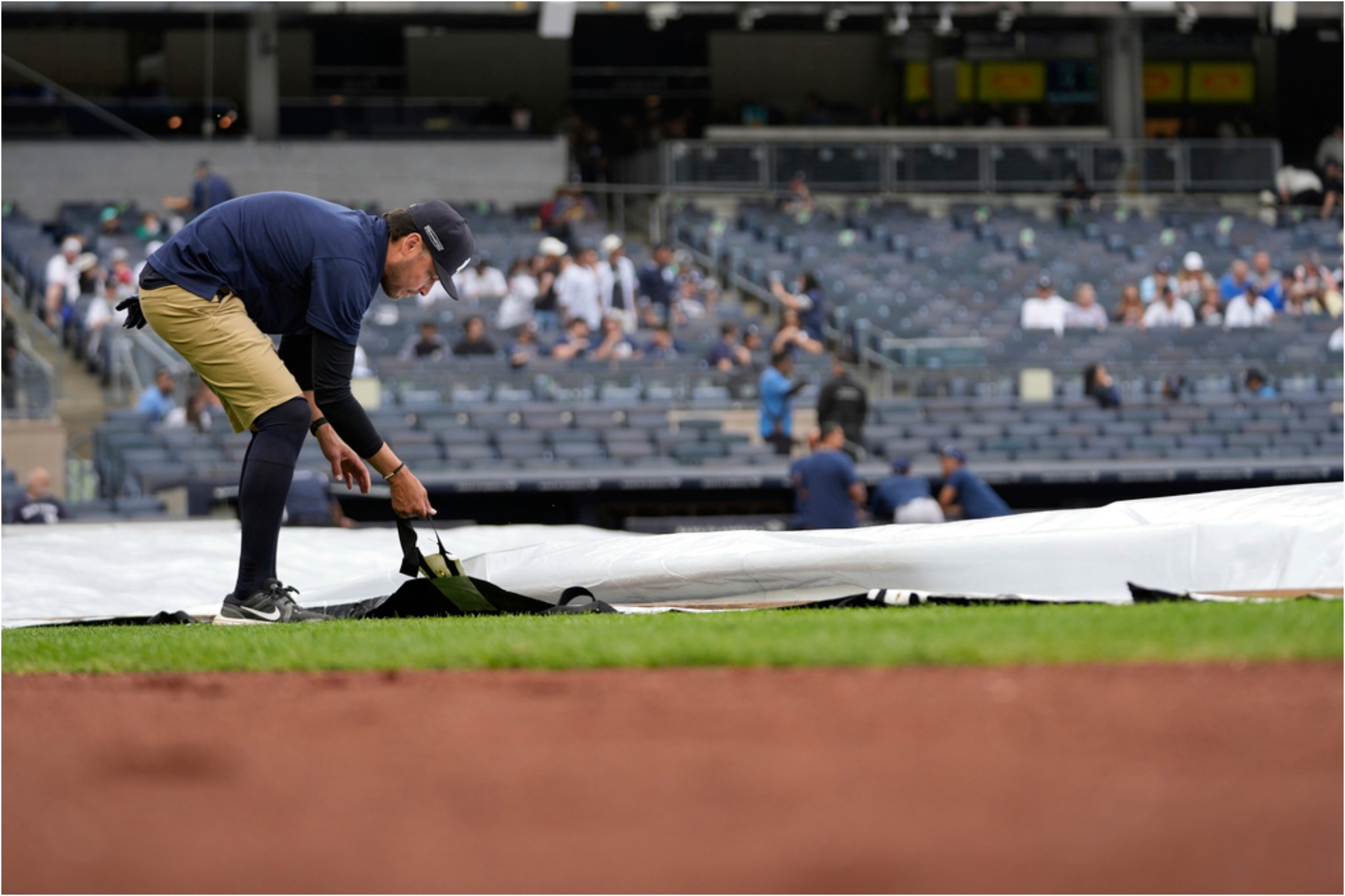 A member of the grounds crew adjusts the rain tarp before a baseball game between the Yankees and the Rays.