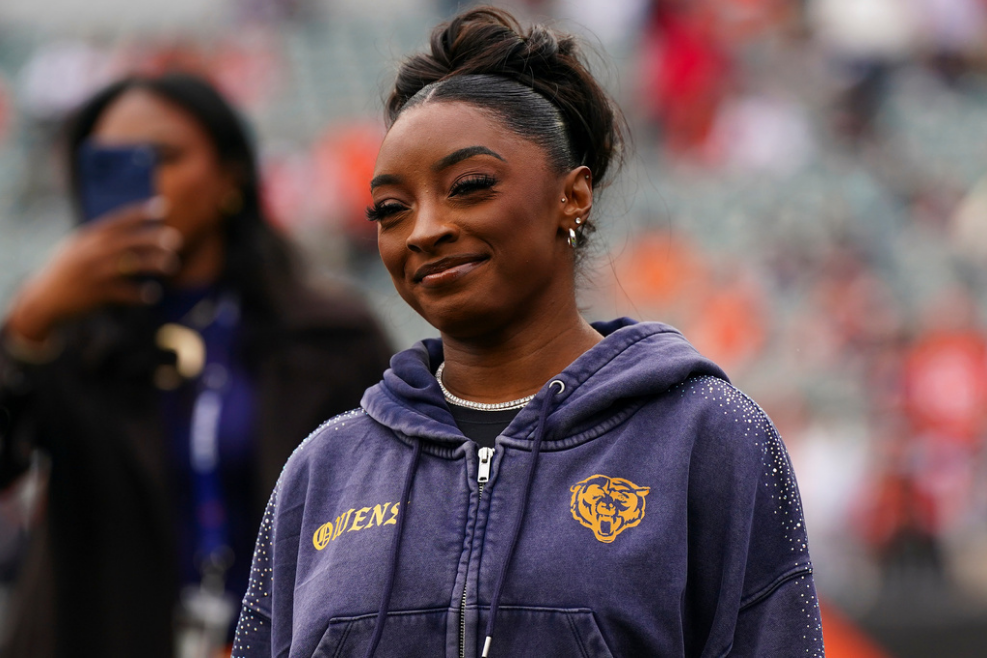 Simone Biles stands on the sideline before an NFL football game