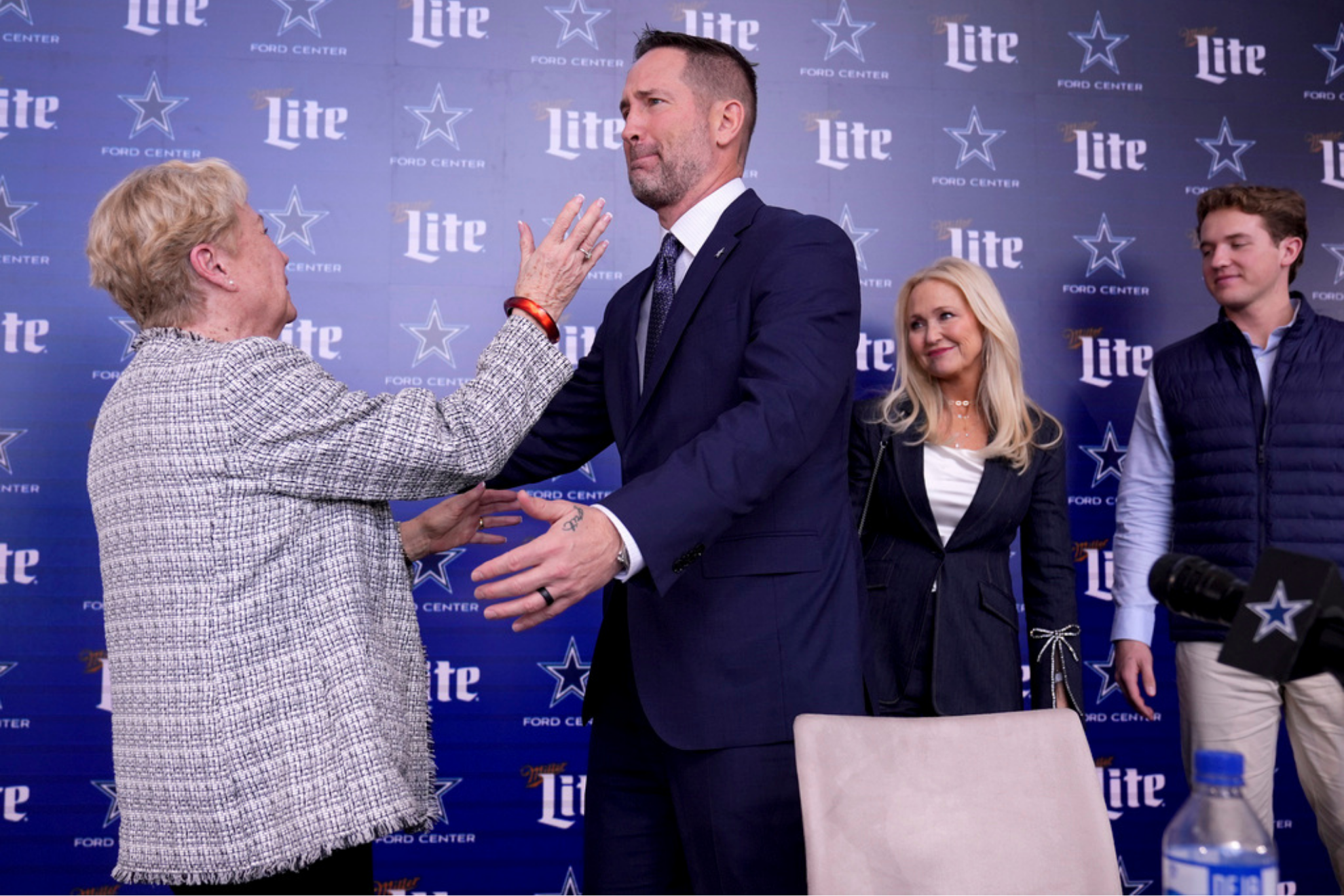 Dallas Cowboys new head coach Brian Schottenheimer, center right, becomes emotional as he reaches to hug his mother, Pat Schottenheimer, left, as his wife Gemmi and son Sutton